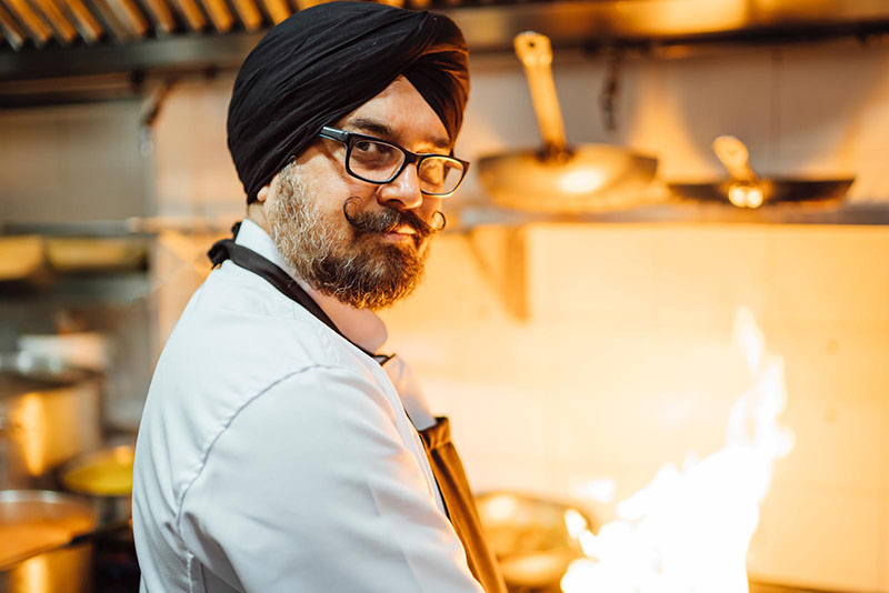 Chef de DOLI con turbante Sikh junto al fuego de la cocina, mostrando su maestría